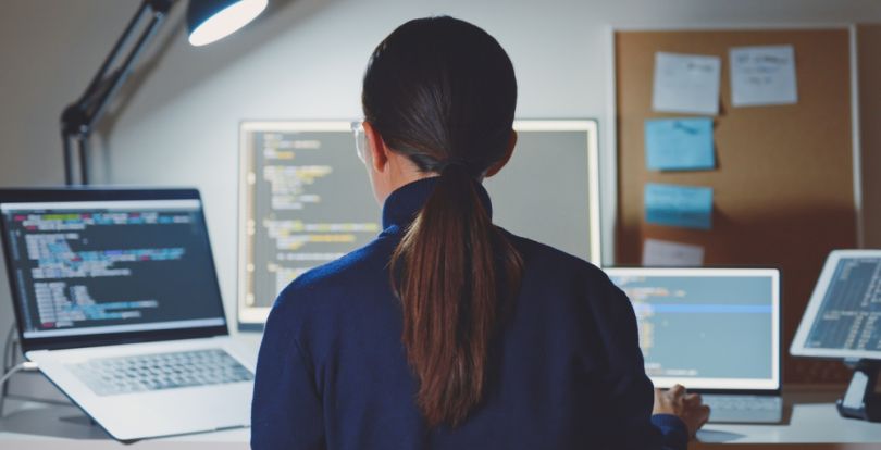 woman sitting in front of several monitors displaying computer code