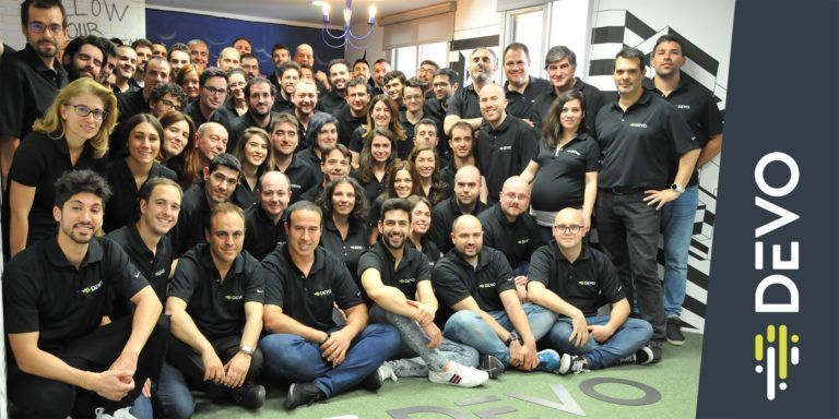 A group shot of Devo's employees in matching polos. The Devo logo takes up part of the right side of the image.