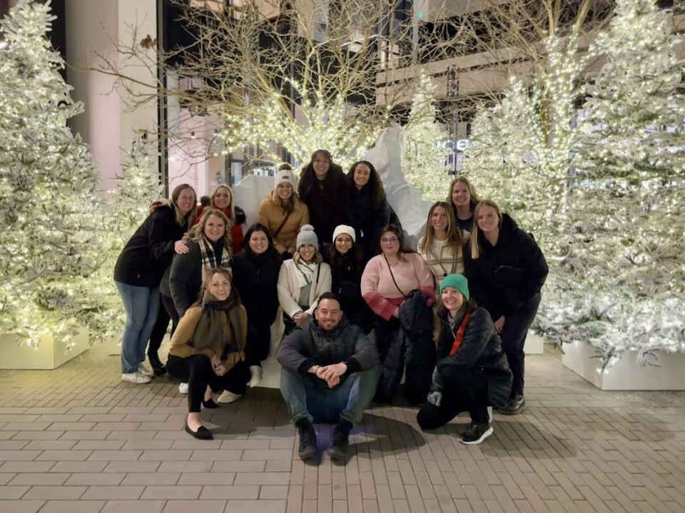  A group of Cohere Health employees clad in winter gear pose for a group photo in front of some decorative winter trees.