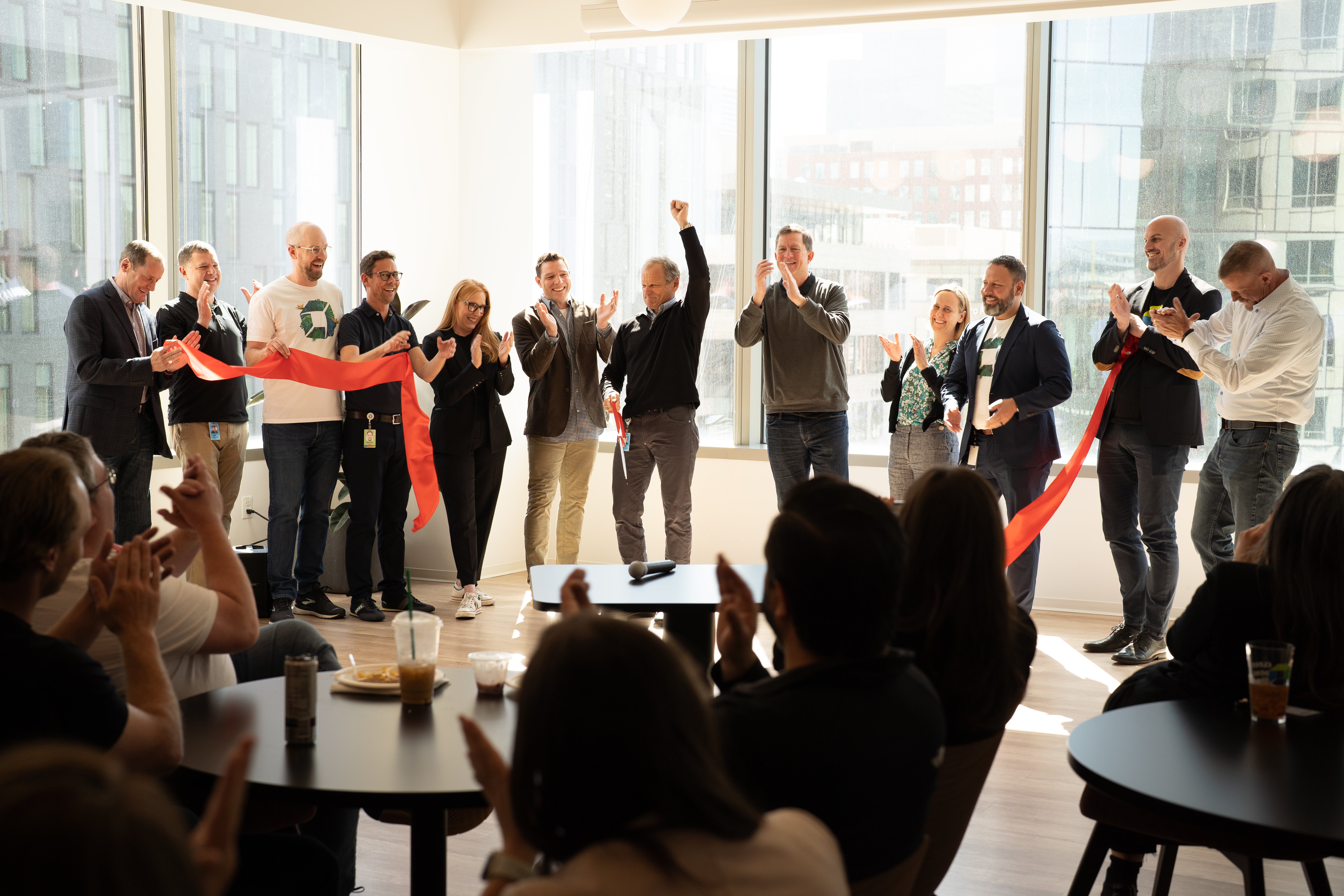 Dynatrace leaders in an office, cutting a ribbon in front of a wall of windows, audience clapping.