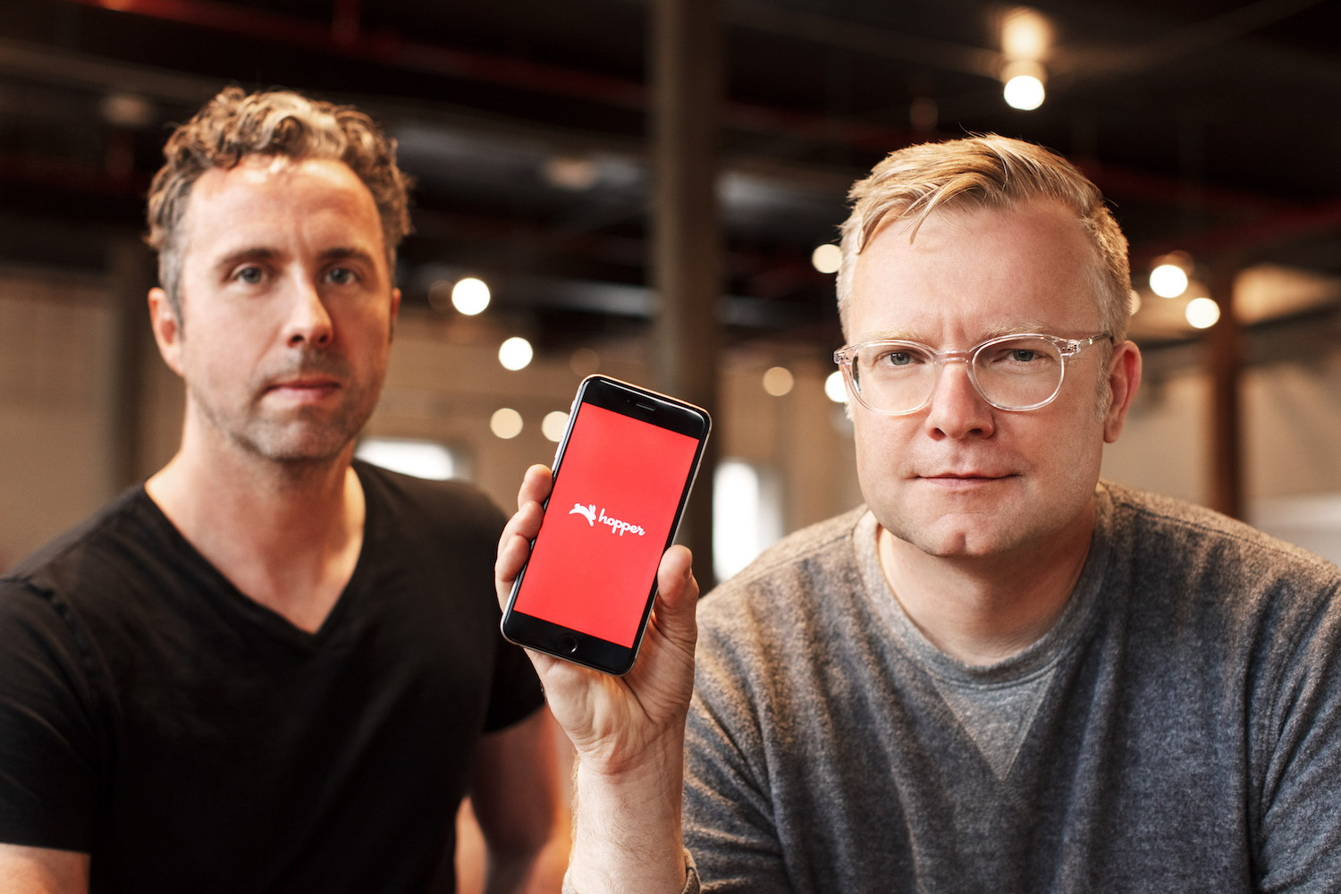 Hopper co-founders pose in an office. CTO Joost Ouwerkerk holds a phone with the Hopper logo on the screen. 