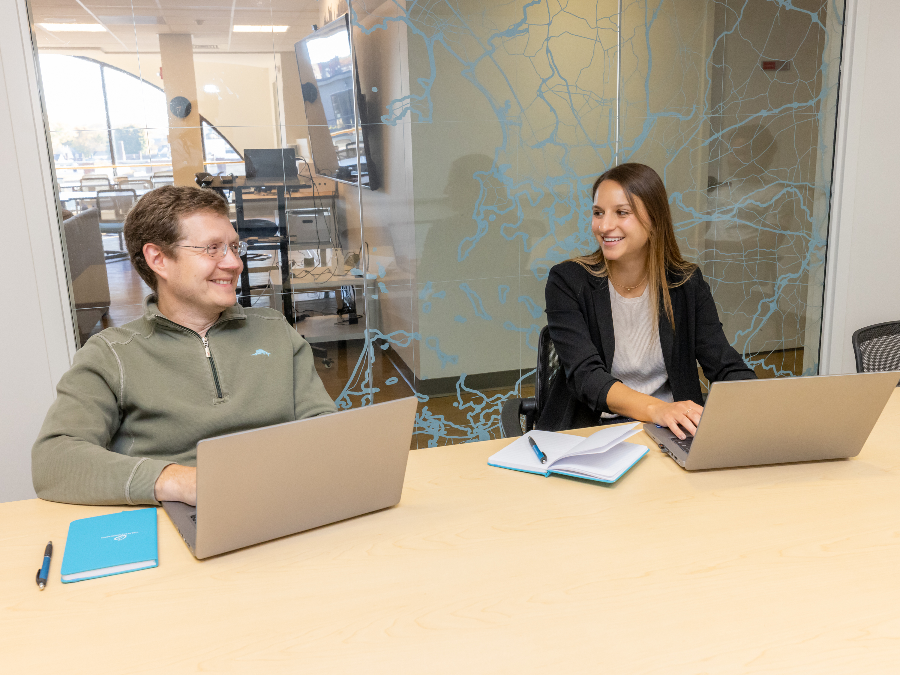 A man and a woman smile at each other while working on laptops