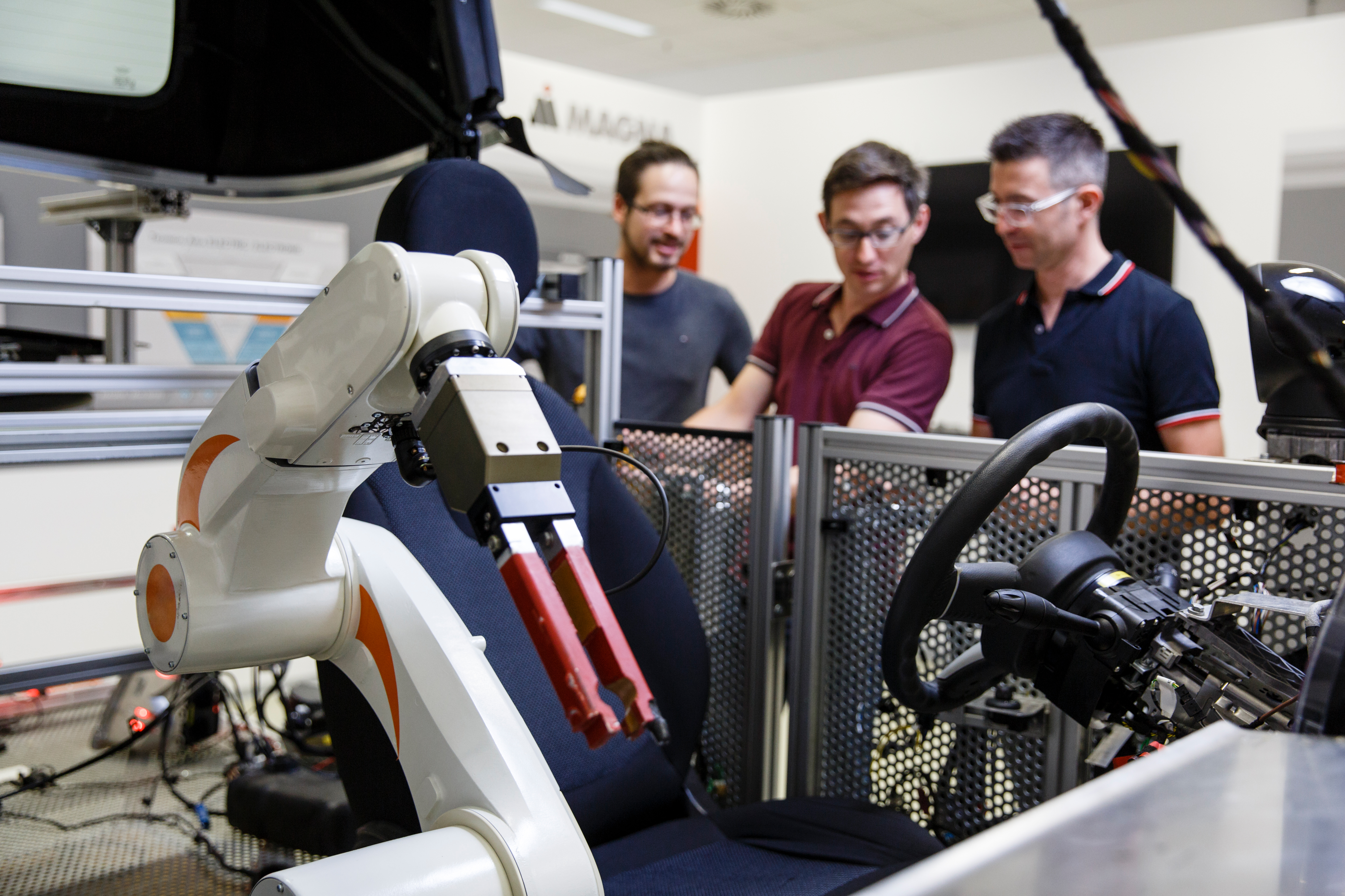 Three Magna engineers look on as robot helps build an automotive machine.