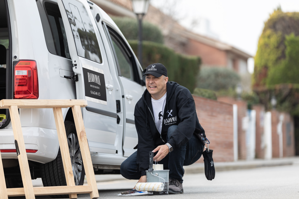 A handyman kneeling down to pick up tools next to a truck with a custom printed car magnet sign on the door