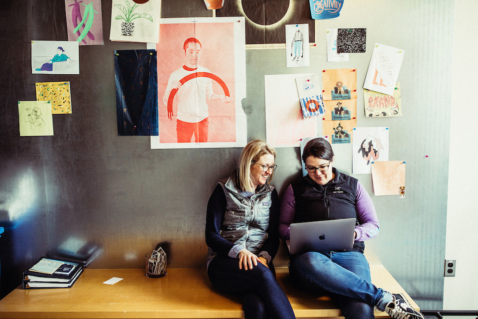 Two Wistia team members sitting on a bench in the office looking at a laptop