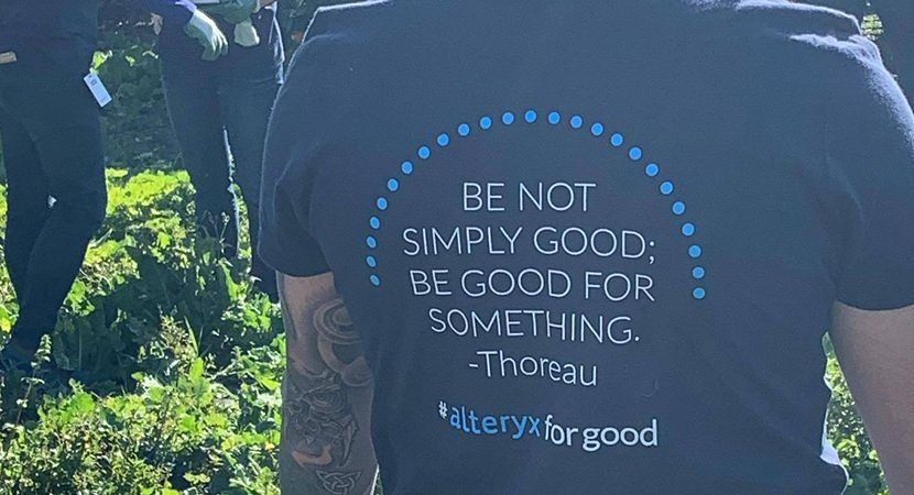 The back of a shirt worn by an Alteryx employee. It has text that reads "BE NOT SIMPLY GOOD; BE GOOD FOR SOMETHING. - Henry David Thoreau." At the bottom of the shirt, it reads #alteryxforgood.
