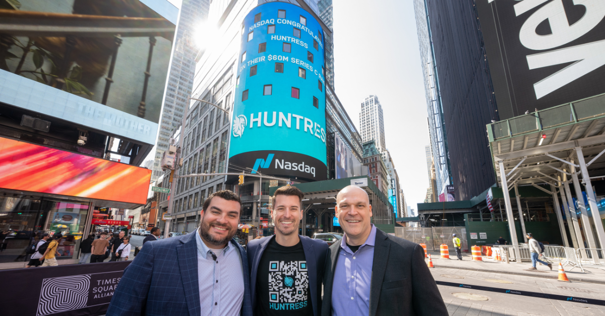 Huntress co-founders stand in Times Square in front of Huntress’ logo on the NASDAQ screen