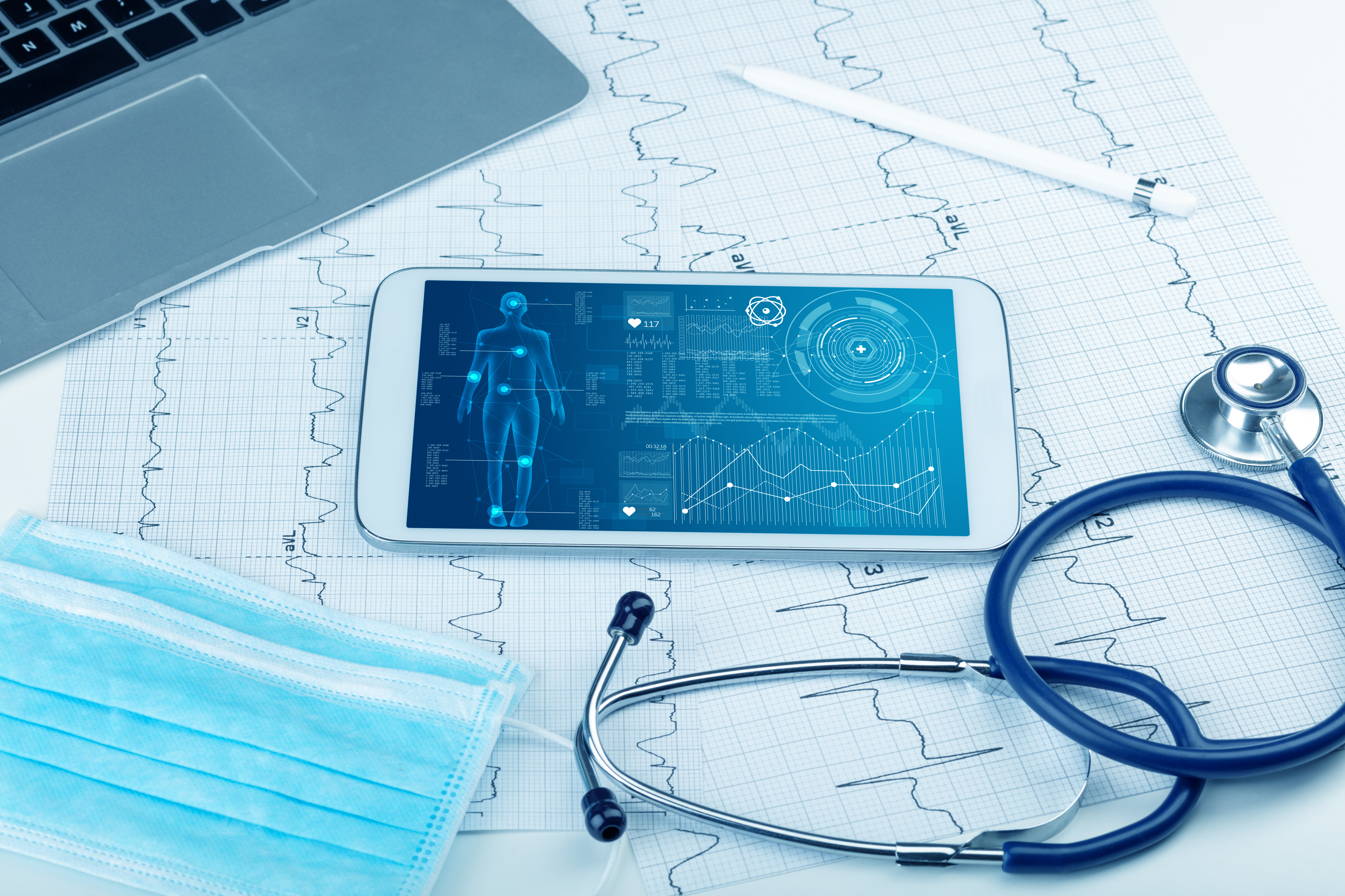 A tablet displays medical data. It sits on a table with various medical equipment. 