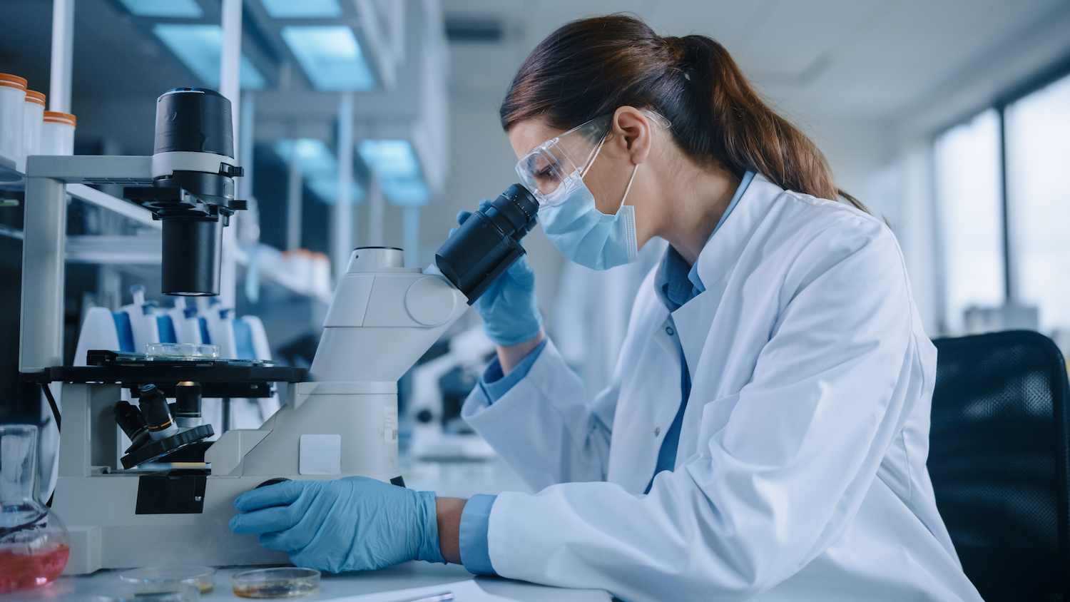 Woman in a lab coat looks into a microscope