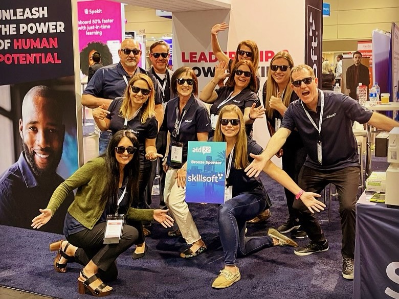 A group of Skillsoft employees pose in sunglasses at a conference booth