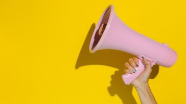 Image of a hand holding up a pink megaphone against a bright yellow background.