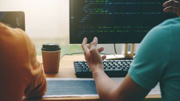 Image of two coworkers discussing the code on computer screens in front of them.