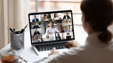 A woman attends a virtual team meeting at home.