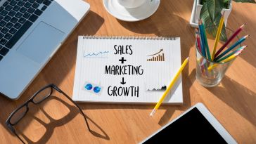 A notebook on a desk with sales + marketing with an arrow pointing to the word growth along with some charts and graphs 