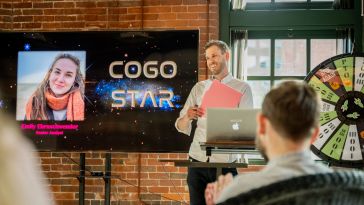 Cogo Labs teammate standing in front of a brick wall and screen presenting to team