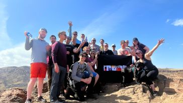 Moov employees hold a flag with the company logo on top of a mountain.