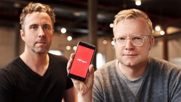 Hopper co-founders pose in an office. CTO Joost Ouwerkerk holds a phone with the Hopper logo on the screen. 
