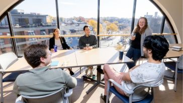 Five people sit around a table in front of a semicircle window