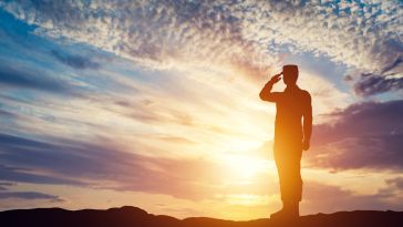 A soldier solutes in front of a sunset.