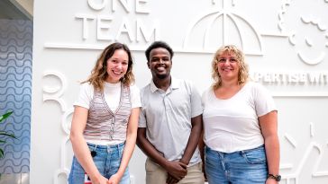 Three toast employees in white shirts standing in front of a white sculpture wall