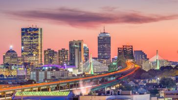 The Boston skyline with bridges and highways at dusk.