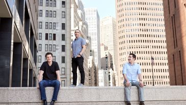 Three NS1 leaders on top of concrete wall amid cityscape background