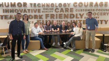 Group photo of Peapod Digital Labs team members sitting in a booth with stylized word wall behind them. 