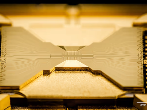 Close-up view of an Ion trap chip, which is a gold rectangle with two flat triangles pointing at each other.