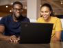 A man and a woman smile at a laptop computer