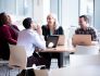 Photo of four colleagues sitting at a table with laptops open, laughing at a joke.