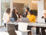 Five Liberty Mutual team members gather at a community table in Liberty Mutual’s common area with laptops, in discussion. 