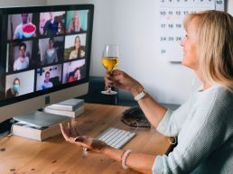 A person drinking wine with their colleagues on a video call.